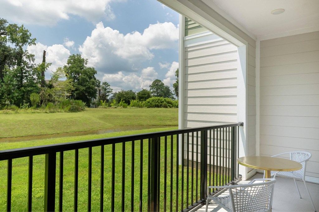 A balcony with a table and chairs overlooking a green field.