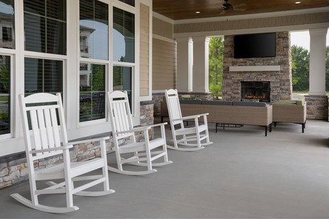 A row of white rocking chairs are lined up in front of a fireplace.