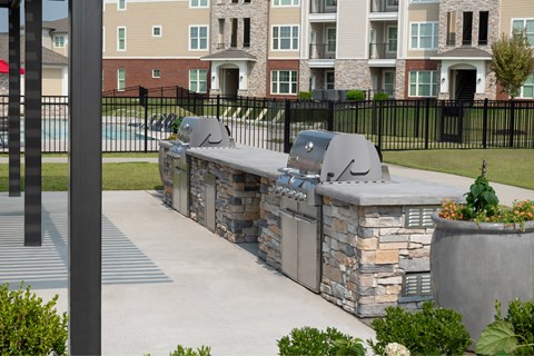 A stone barbecue grill is in the middle of a concrete patio.