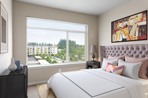 A bedroom with a large bed and a view of a residential area outside the window.