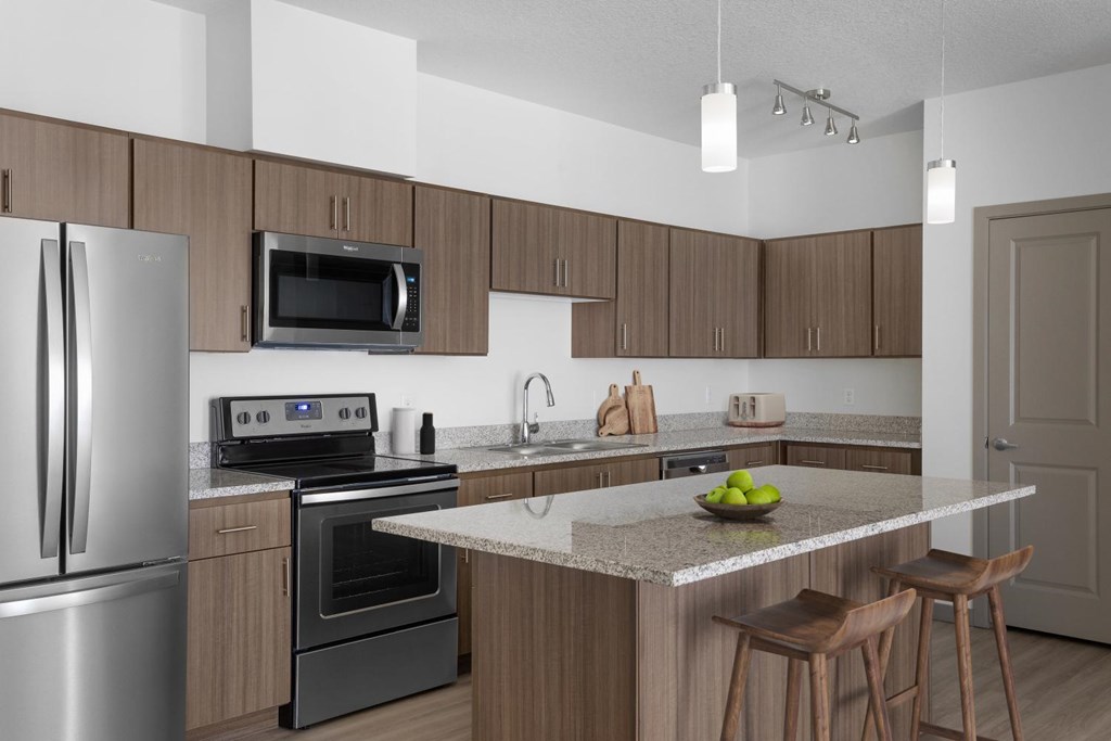 A modern kitchen with a stainless steel refrigerator, microwave, oven, and a marble countertop.