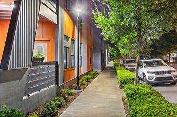 A sidewalk runs down the middle of a street lined with parked cars.