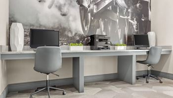 A modern office with a large poster on the wall and two computers on the desks.