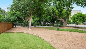 A park with a green lawn and a dirt area with a tree in the middle.