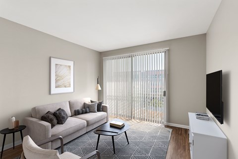 A living room with a grey couch, a black chair, a small table, a television, and a window with blinds.