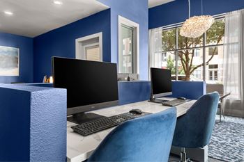 A blue chair is in front of a desk with a computer monitor and keyboard.