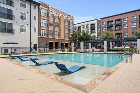 A pool surrounded by chairs and buildings.