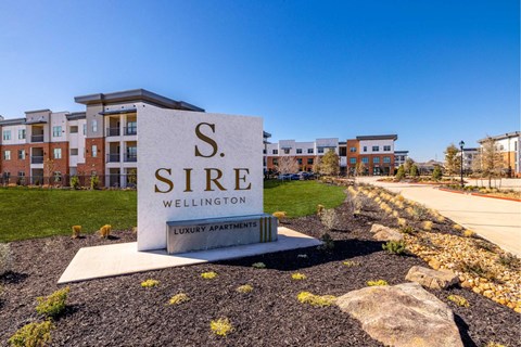 A sign for S. Sire Wellington luxury apartments is in the foreground with apartment buildings in the background.