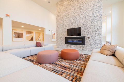 A living room with a white couch, a pink ottoman, and a television mounted on the wall.