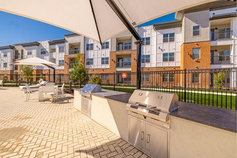 A patio with a grill and chairs under a white awning.