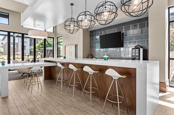 A modern kitchen with a bar area and white stools.