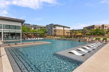 A large swimming pool with lounge chairs is surrounded by buildings.