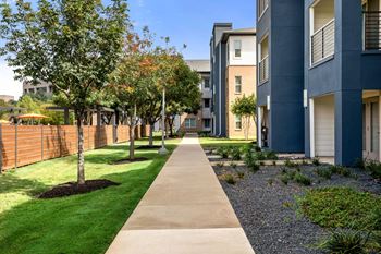 A long concrete walkway separates the grassy area from the apartment buildings.