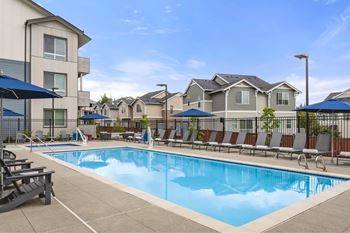 A swimming pool surrounded by lounge chairs and umbrellas in a residential area.