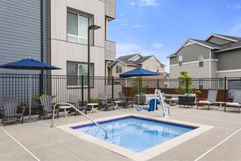 A swimming pool in a residential area surrounded by chairs and umbrellas.
