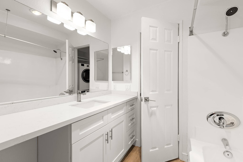 A white bathroom with a sink, mirror, and shower.