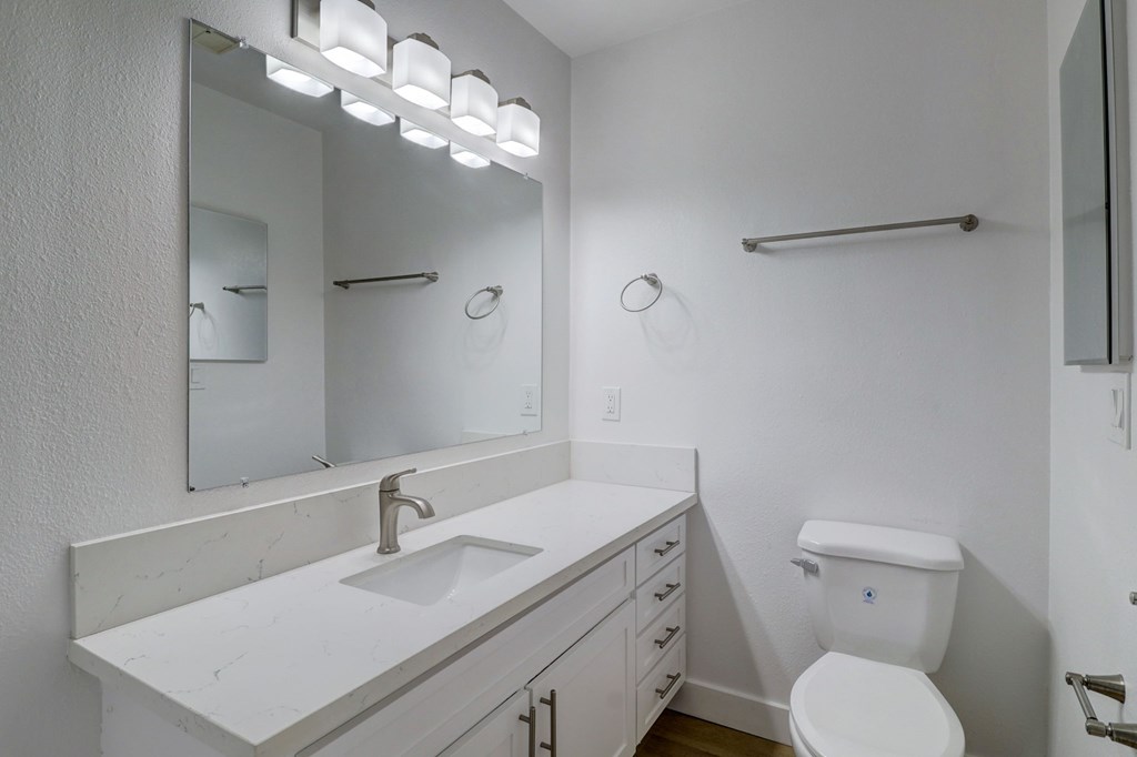 A white bathroom with a sink, toilet, and mirror.