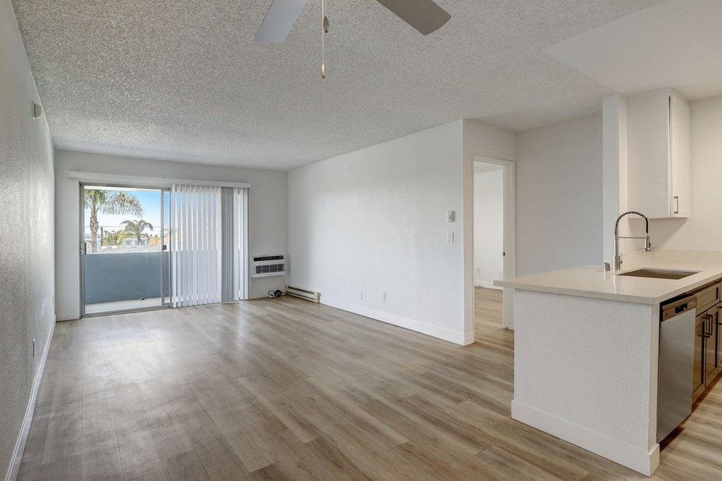 A spacious living room with a kitchenette and sliding glass doors leading to a balcony.