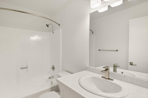A white bathroom with a sink, mirror, and bathtub.