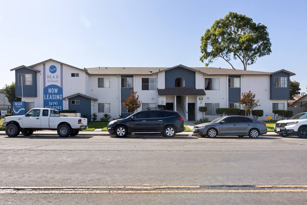 A white pickup truck is parked in front of a blue and white apartment building.