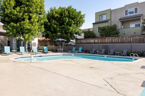 A swimming pool surrounded by trees and chairs.