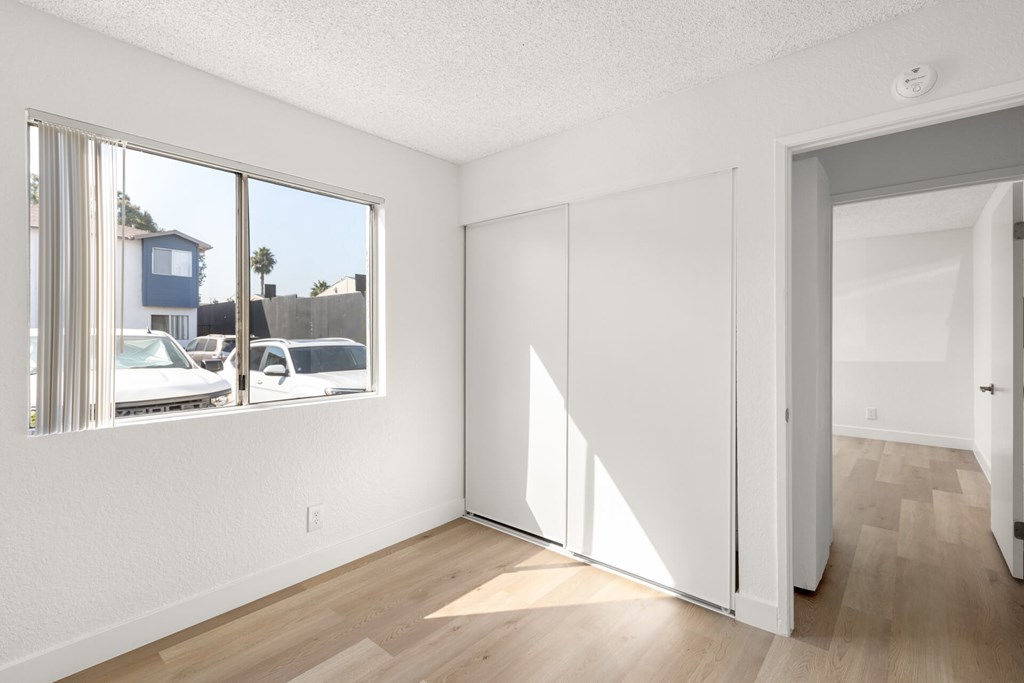 A room with a white wall and a window with a view of a house and cars outside.