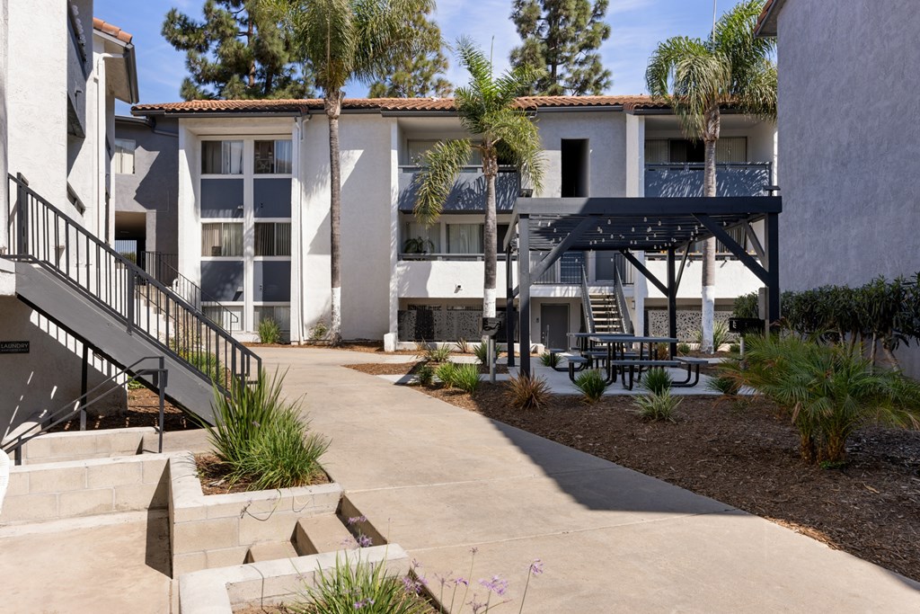 A patio area with a table and chairs is surrounded by a building and trees.