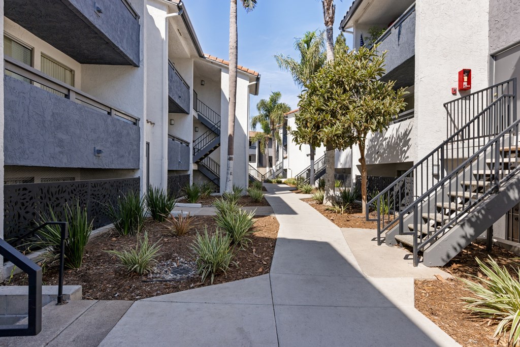 A concrete walkway leads through a landscaped courtyard between two apartment buildings.