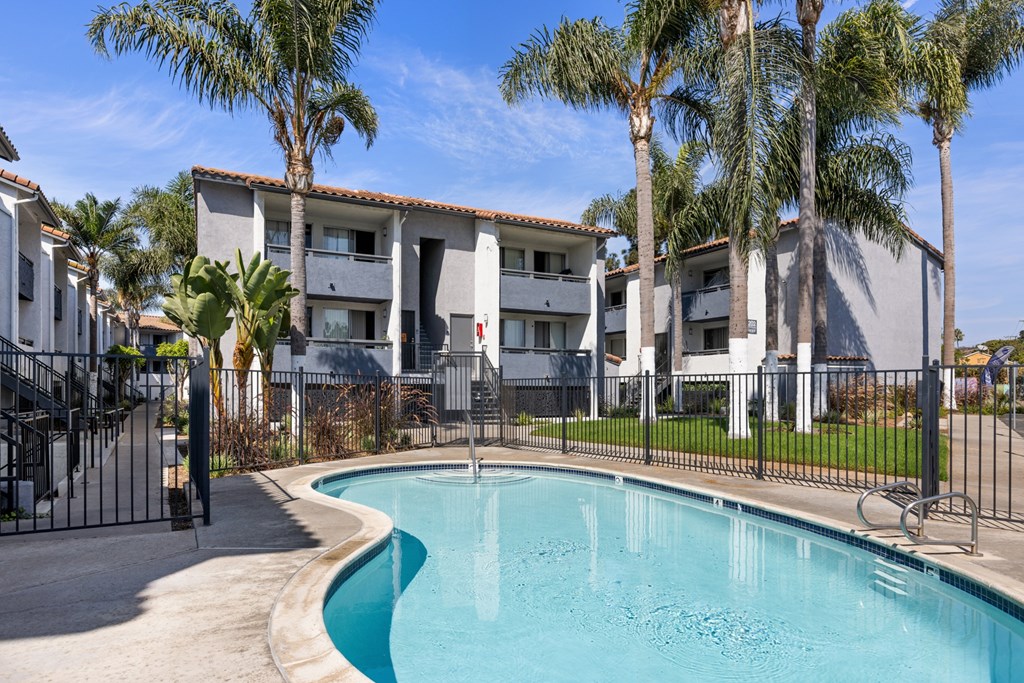 A swimming pool in front of a building surrounded by palm trees.