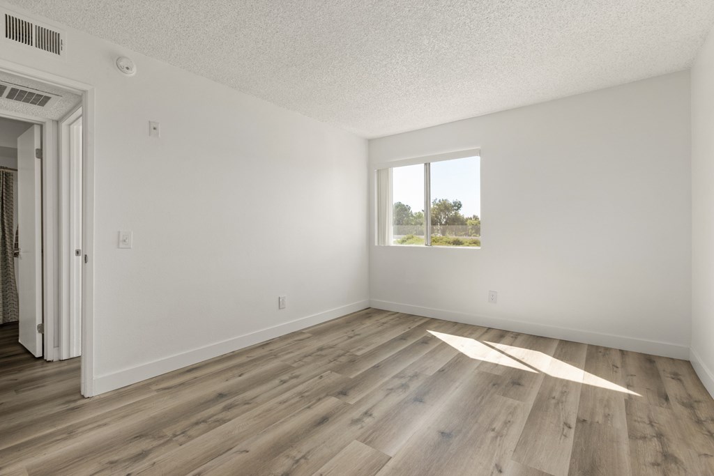 A room with wooden flooring and a window overlooking a field.