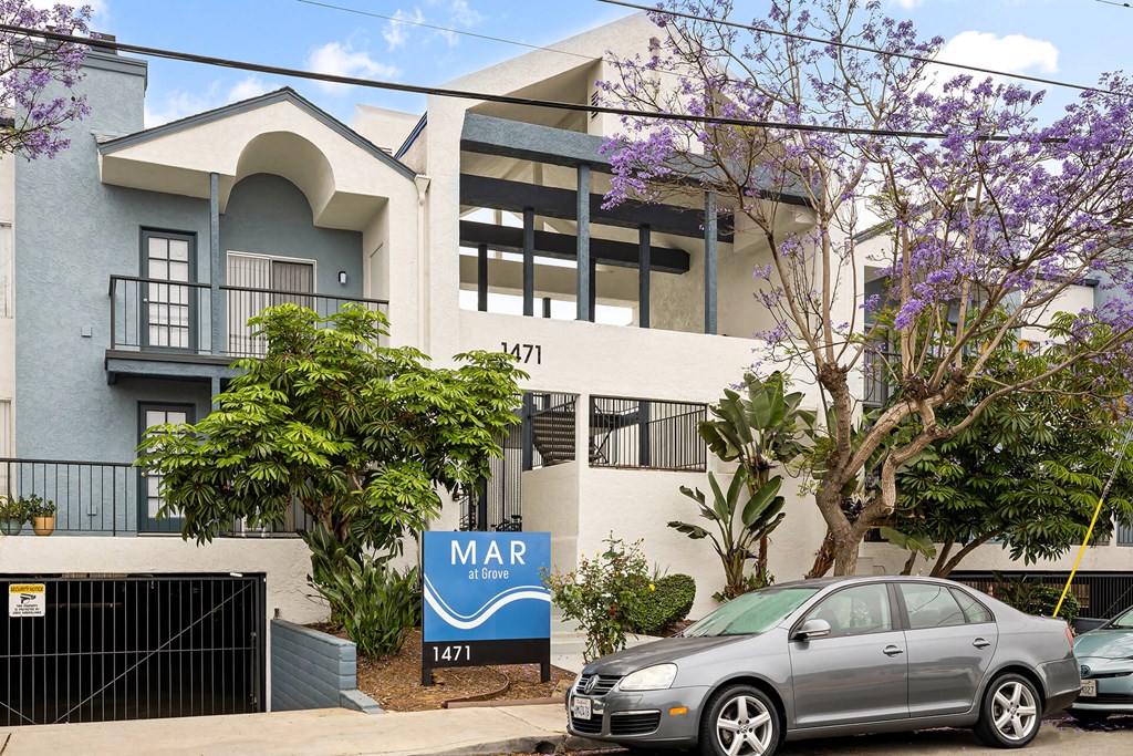 A grey car is parked in front of a building with a sign that says