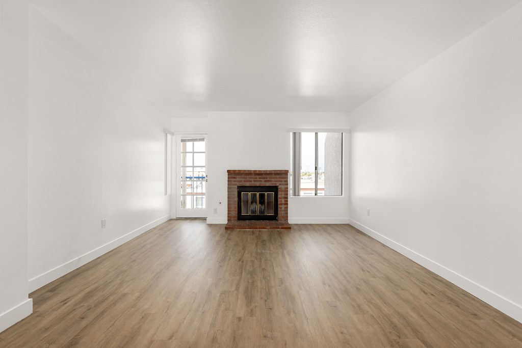 A large empty room with a fireplace and wood flooring.