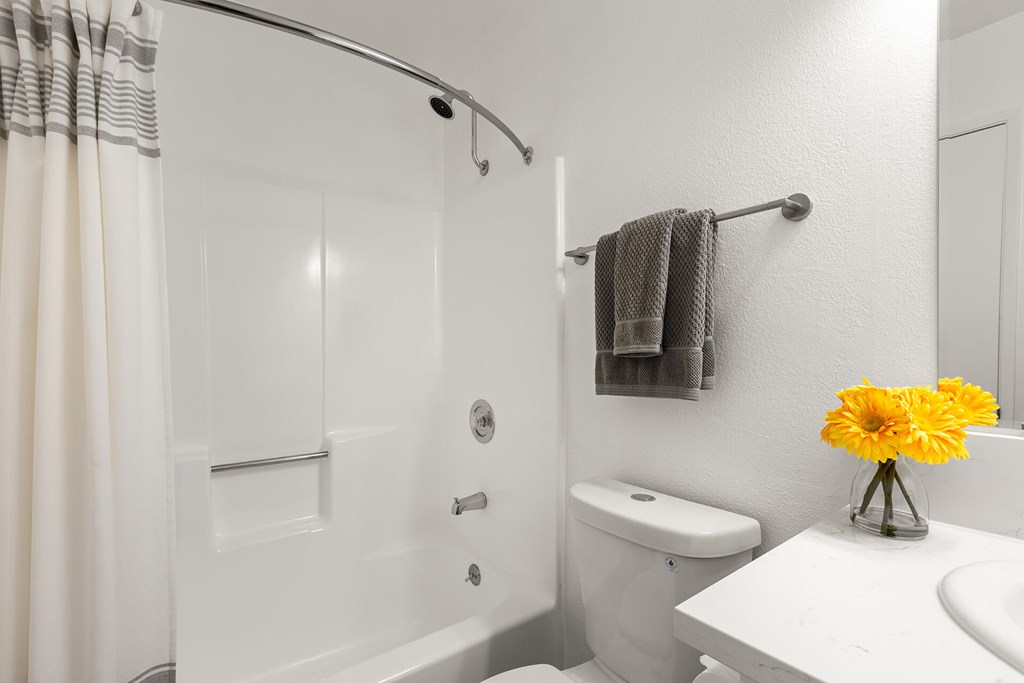 A white bathroom with a towel rack and a vase of yellow flowers.