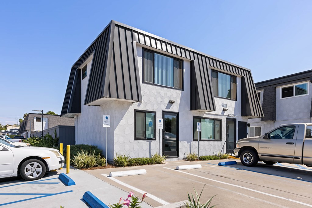 A white car is parked in a parking lot in front of a building with a black and white striped facade.