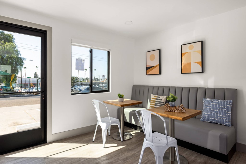 A white chair is in front of a grey couch with a table and two chairs in between.