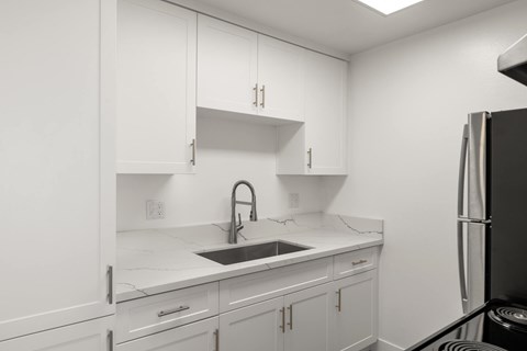 A kitchen with white cabinets and a black refrigerator.
