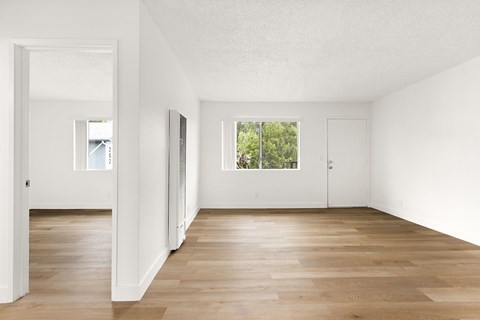 A room with white walls and wooden flooring with a window.