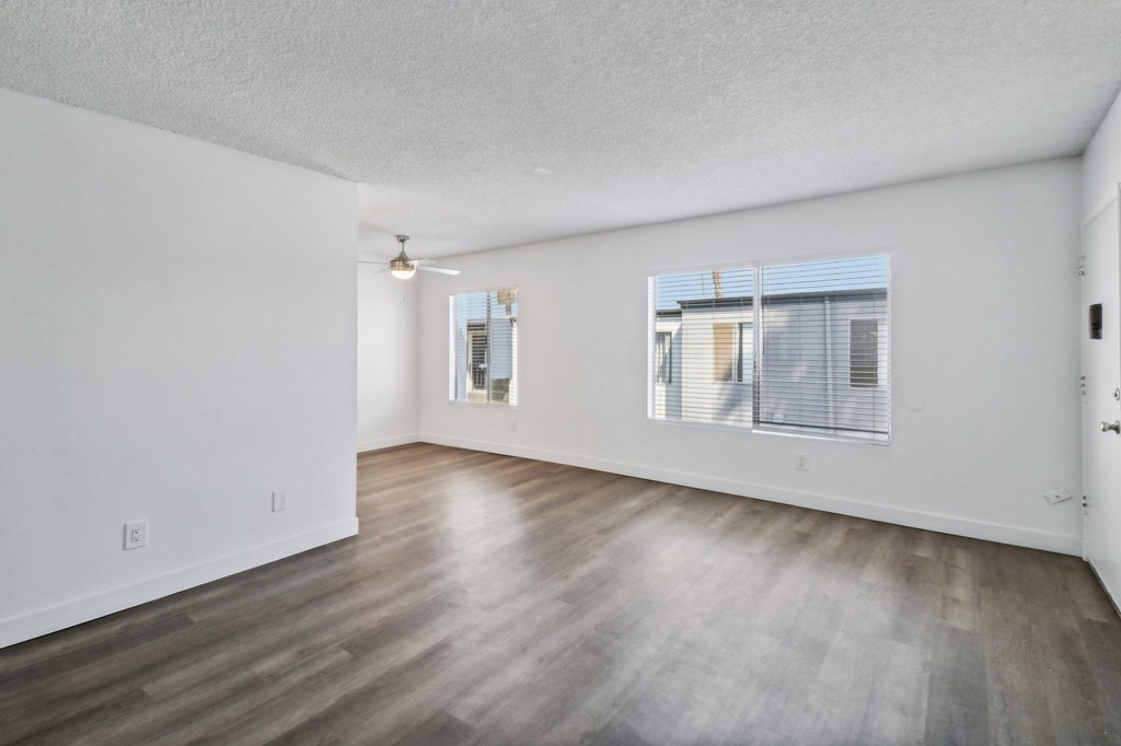 A spacious room with wooden flooring and a window with blinds.