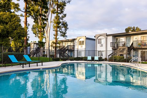 A swimming pool in front of apartment buildings with trees in the background.