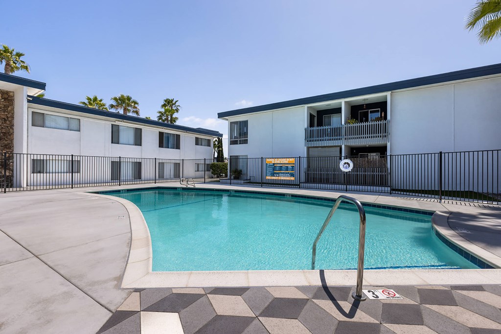 A swimming pool in front of a building with a black fence around it.