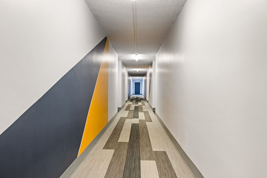 A long hallway with a carpeted floor and a wall on the left side.