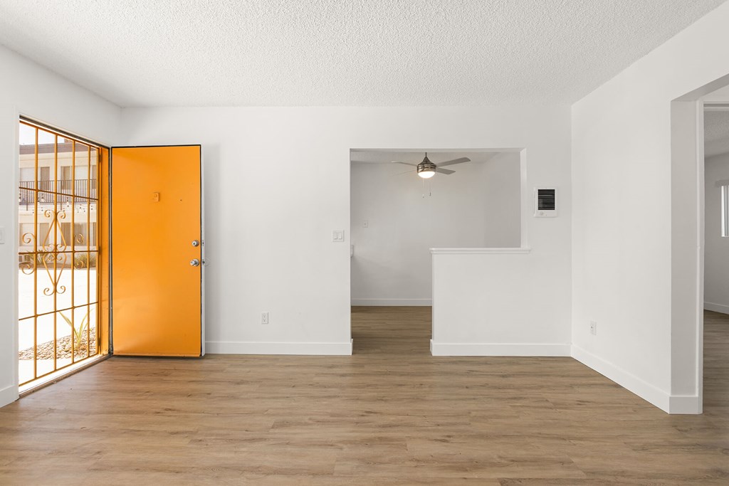 A room with a wooden floor and white walls, with a ceiling fan and a door leading to a balcony.