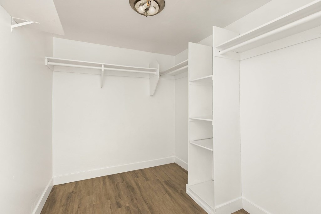 A white room with a wooden floor and a white closet with shelves.