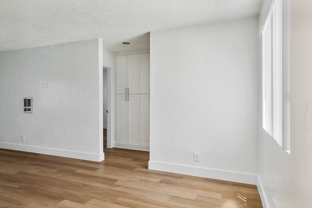 A room with white walls and wooden flooring with a doorway leading to another room.