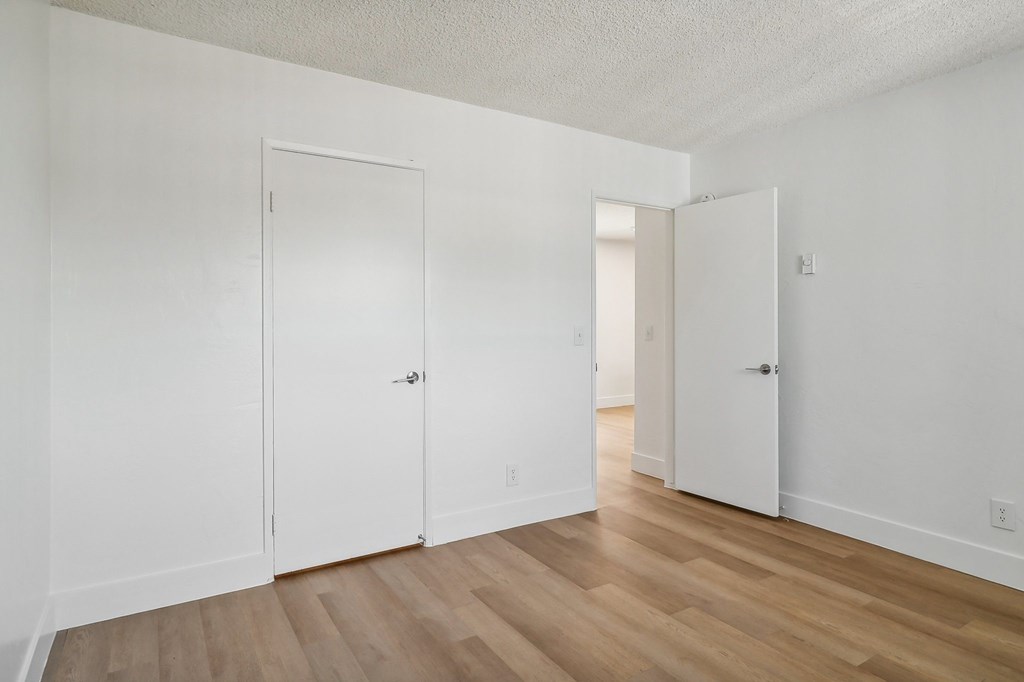 A room with white walls and wooden flooring with two doors.