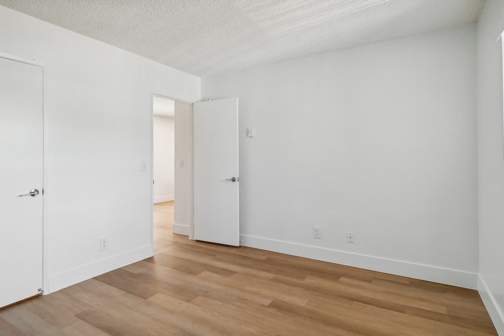 A room with white walls and wooden flooring with two doors.