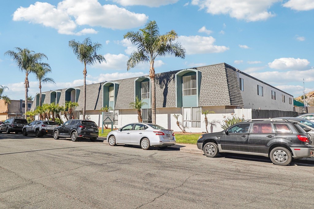 A parking lot with cars and a building with palm trees in the background.