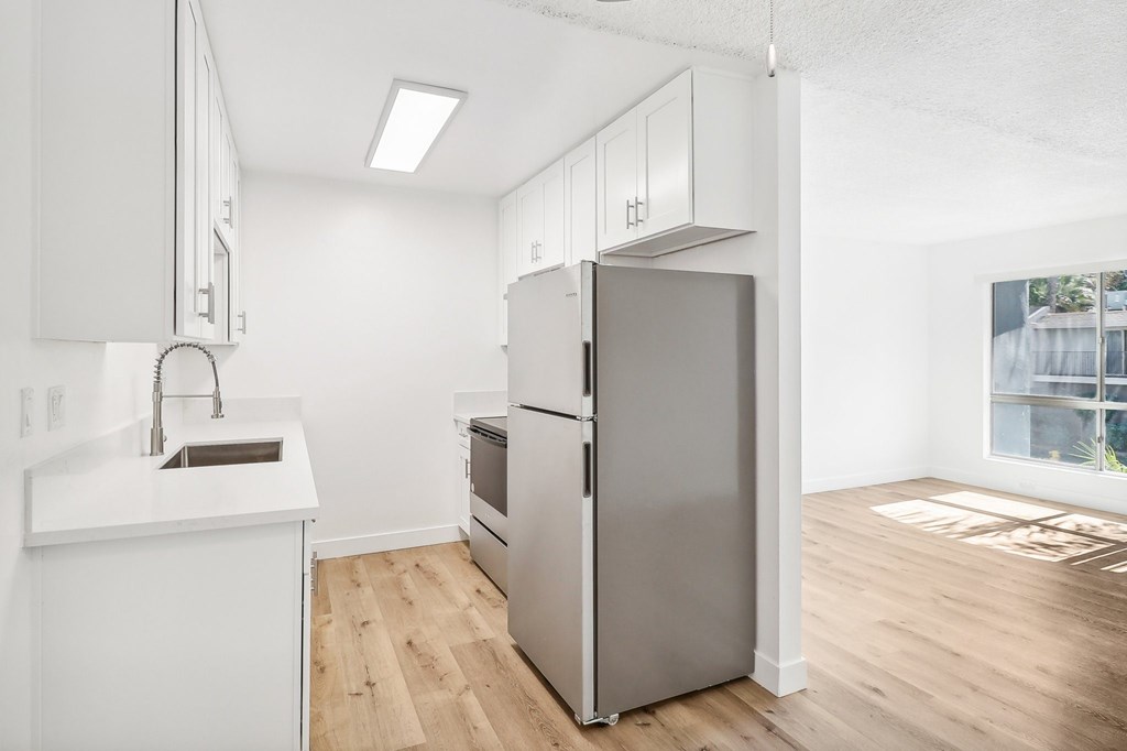 A kitchen with a refrigerator, sink, and cabinets.