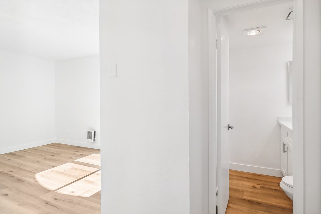 A white room with a wooden floor and a doorway leading to another room.