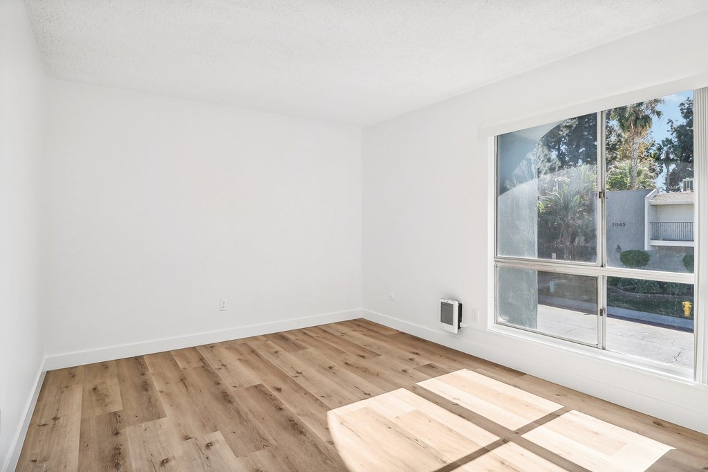 A room with a window showing a view of a house and trees outside.